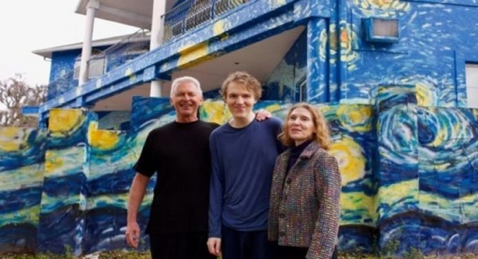 Descrição da imagem #PraCegoVer: Imagem no formato retangular, na horizontal. O jovem autista e seus pais, em frente à casa onde moram, que teve a fachada pintada com referências de uma das obras de Van Gogh. Fim da descrição.