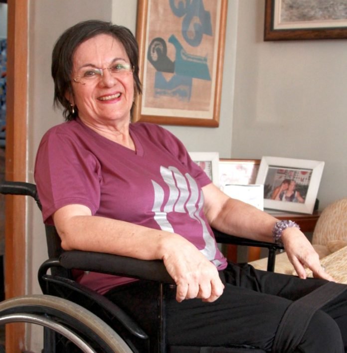 Descrição de imagem #PraCegoVer: Imagem no formato retangular, na horizontal. Maria da Penha está sentada em sua cadeira de rodas. Ela é uma mulher morena, de pele clara, e cabelos pretos, lisos e curtos. Maria da Penha está sorrindo. Fim da descrição.