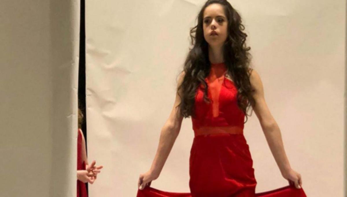 Descrição da imagem #PraCegoVer: Imagem no formato retangular, na horizontal. A modelo com síndrome de Down, Marian Avila, durante desfile no New York Fashion Week. Ela é uma jovem morena, de cabelos castanhos, que estão cacheados na foto. Marian usa um vestido vermelho. Fim da descrição. Descrição da imagem #PraCegoVer: Imagem no formato retangular, na horizontal. A modelo com síndrome de Down, Marian Avila, durante desfile no New York Fashion Week. Ela é uma jovem morena, de cabelos castanhos, que estão cacheados na foto. Marian usa um vestido vermelho. Fim da descrição.