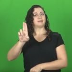 Descrição da imagem #PraCegoVer: Imagem no formato retangular, na horizontal. Uma mulher está fazendo um sinal em Libras. Ela é morena, tem a pele clara e cabelos pretos, compridos e cacheados. Fim da descrição.