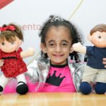 Descrição da imagem #PraCegoVer: Imagem no formato retangular, na horizontal. A menina Luara Crystal, criança símbolo do Teleton 2018. Ela.é uma menina morena e tem cabelos cacheados. Luara está segurando os mascotes do Teleton, Tonzinho e Nina. Luara sorri. Fim da descrição.