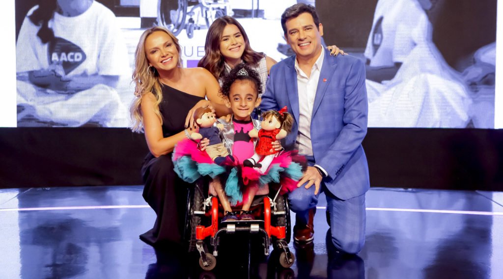 Descrição da imagem #PraCegoVer: Imagem no formato retangular, na horizontal. Eliana, Maisa e Celso Portiolli, com Luara Cristal. Fim da descrição.