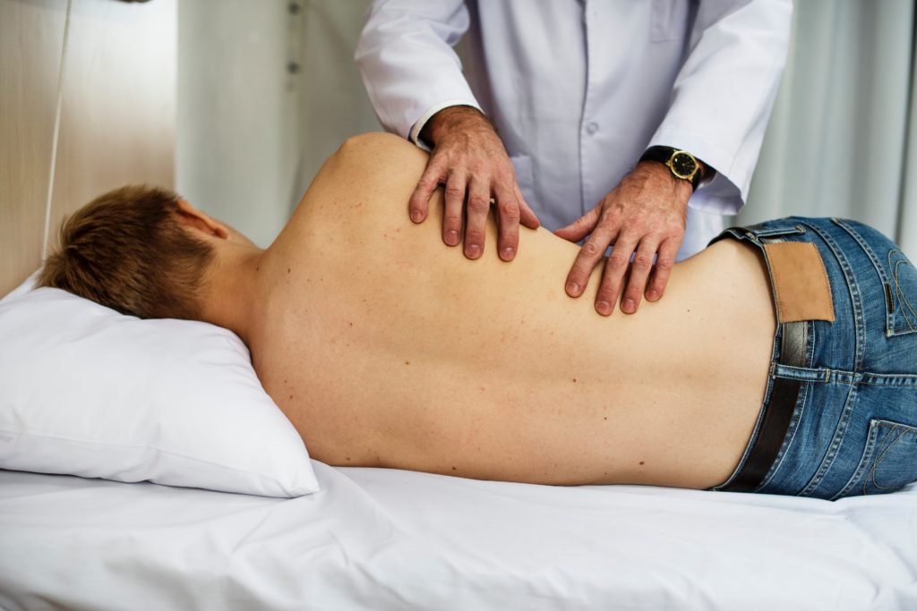 Descrição da imagem #pracegover: Um homem está deitado em uma maca, sem camisa, e está sendo examinado por um médico. Fim da descrição.
