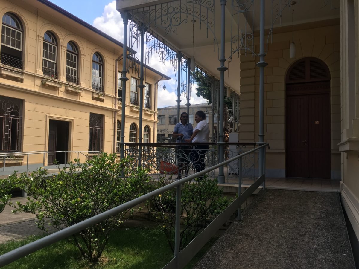 Descrição da imagem #PraCegoVer: Imagem no formato retangular, na horizontal. O jornalista Ismael da Silva na entrada do Museu da Energia de São Paulo, ao lado da educadora do museu. Eles estão conversando ao lado envoltos a uma moldura formada pelas paredes do museu. Fim da descrição.