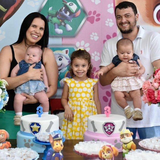 Descrição da imagem #PraCegoVer: Imagem no formato retangular, na horizontal. Raquel e o marido Daniel com as três filhas: Laura está na sua frente e as gêmeas Luiza e Lívia estão no colo dos pais. Fim da descrição.