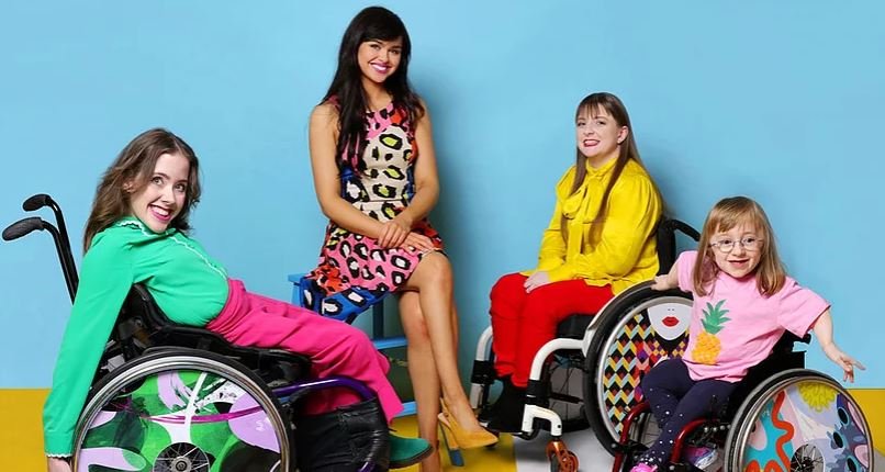 Descrição da imagem #PraCegoVer: Imagem no formato retangular, na horizontal. Imagem de divulgação das rodas personalizadas da marca Izzy Wheels. Nela estão 4 pessoas, sendo as irmãs Ailbhe e Izzy e mais uma mulher e uma criança, que estão sentadas em suas cadeiras de rodas. Fim da descrição.