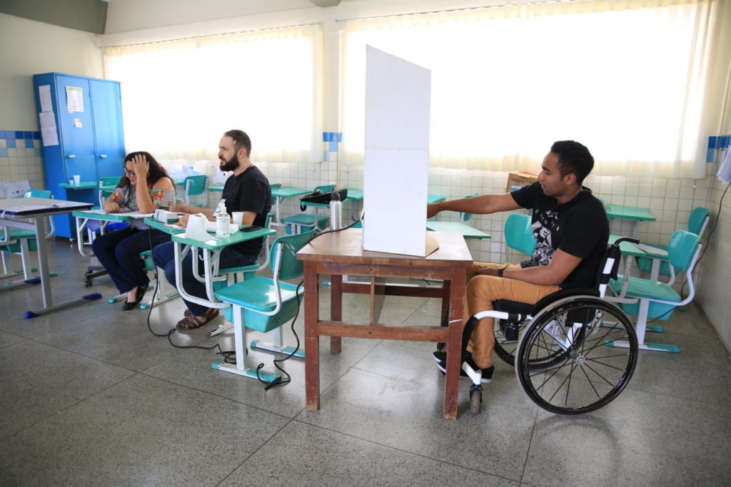 Descrição da imagem: foto de um homem com deficiência física (cadeirantes) durante a votação em uma seção eleitoral acessível. Fim da descrição.