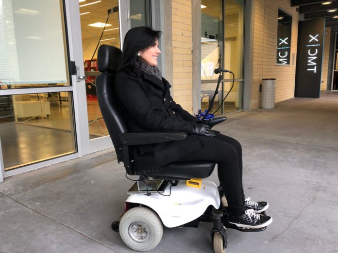 Descrição da imagem #PraCegoVer: Imagem no formato retangular, na horizontal. Uma mulher está em sua cadeira de rodas e usa o kit Wheelie 7 para movimentar a cadeira com movimentos do rosto. Ela é morena, de pele clara e cabelos pretos. E está usando uma roupa preta. Fim da descrição.