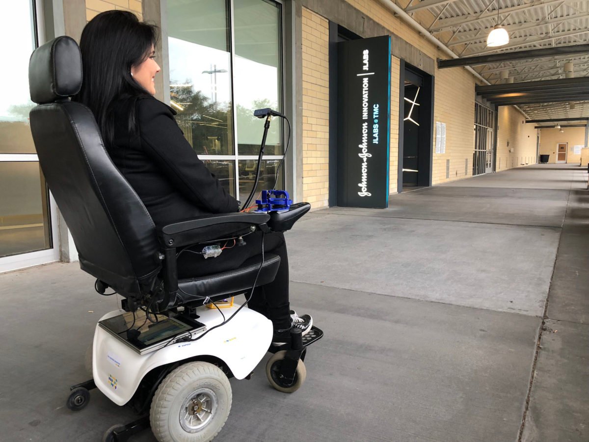 Descrição da imagem #PraCegoVer: Imagem no formato retangular, na horizontal. Uma mulher está em sua cadeira de rodas e usa o kit Wheelie 7 para movimentar a cadeira com movimentos do rosto. Ela é morena, de pele clara e cabelos pretos. E está usando uma roupa preta. Fim da descrição.