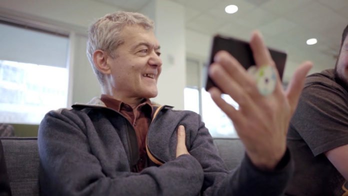Descrição da imagem #PraCegoVer: Imagem no formato retangular, na horizontal. O pesquisador Dimitri, durante teste do app. Ele está sentado e segura um celular. Ele é um homem idoso, com pele clara e cabelos grisalhos, curtos. Dimitri está sorrindo. Fim da descrição.