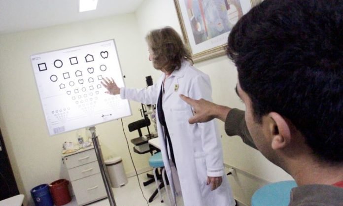 Descrição da imagem #PraCegoVer: Imagem no formato retangular, na vertical. Um homem está fazendo um exame ocular. Fim da descrição.