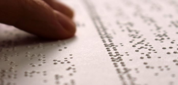 Descrição da imagem #PraCegoVer: Dedos fazem a leitura em braille em um documento impresso. Fim da descrição.