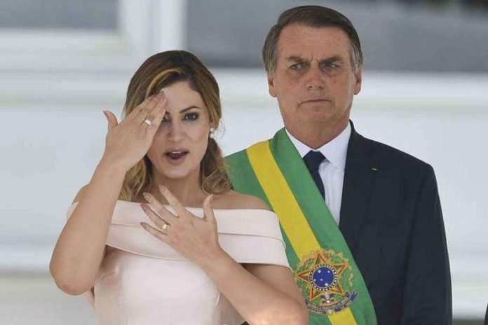 Descrição da imagem #PraCegoVer: Imagem no formato retangular na horizontal. A primeira-dama Michelle Bolsonaro está discursando em Libras durante a posse do novo presidente, Jair Bolsonaro, que está ao seu lado esquerdo. Michelle é uma mulher loira e seus cabelos são na altura dos ombros. Sua pele é branca e ela usa um vestido rosa claro. Michelle está fazendo um sinal em Libras. Fim da descrição.