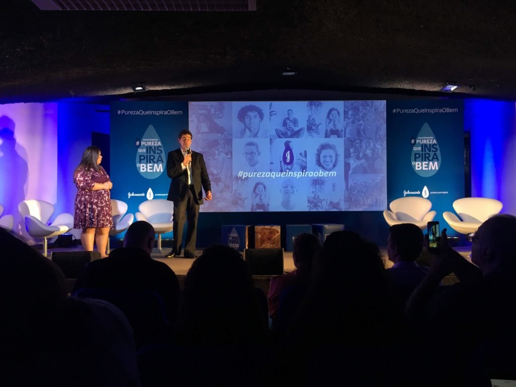 Descrição da imagem #PraCegoVer: Imagem no formato retangular, na horizontal. Uma mulher e um homem estão de pé em um palco, durante o evento. Fim da descrição.