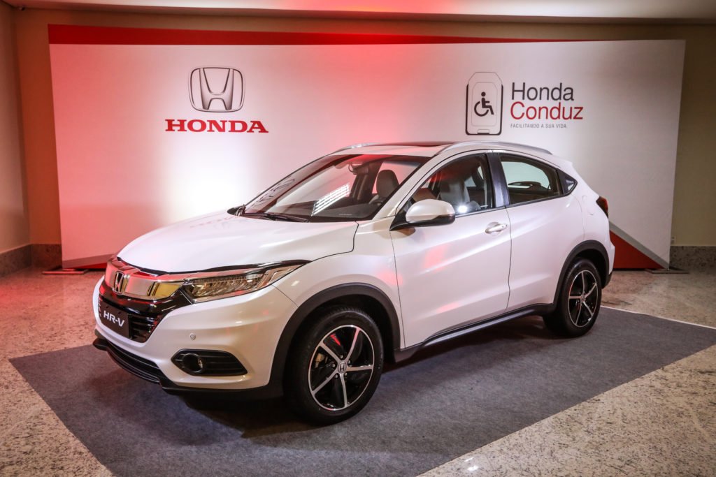 Descrição da imagem #PraCegoVer: Novo HR-V da Honda. O carro é um modelo SUV Compacto, branco. Ele está de lado. Ao fundo estão os logos da montadora Honda e do Programa Honda Conduz. Fim da descrição.