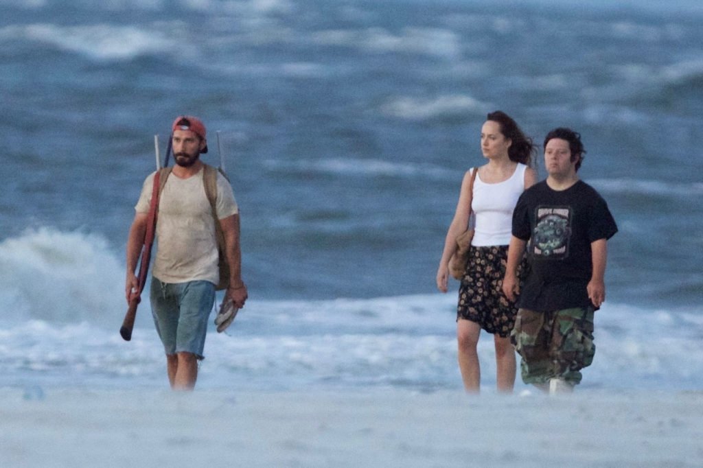 Descrição da imagem #PraCegoVer: Os três atores do filme estão caminhando em uma praia. Eles estão dentro do mar. Fim da descrição.