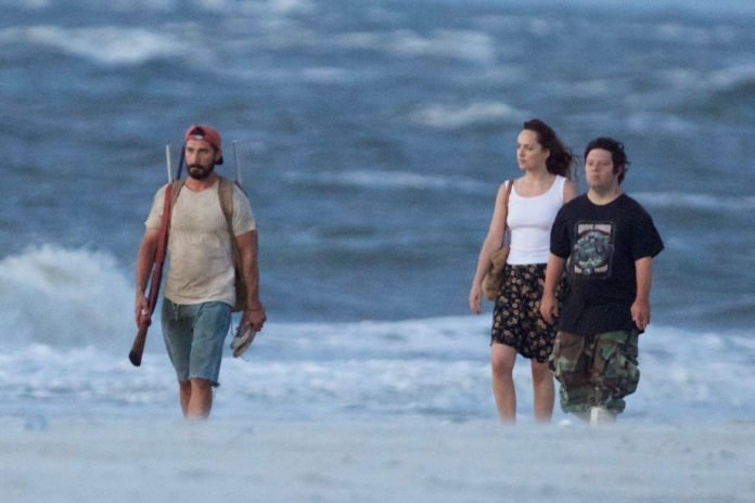 Descrição da imagem #PraCegoVer: Os três atores do filme estão caminhando em uma praia. Eles estão dentro do mar. Fim da descrição.