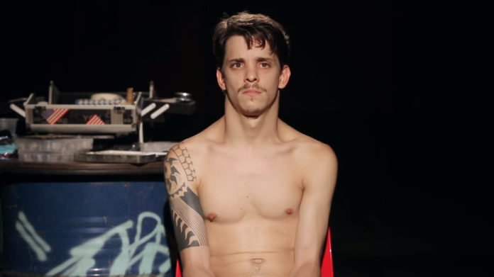 Descrição da imagem #PraCegoVer: Daniel está sentado em uma cadeira. Ele está sem camisa. Daniel é um rapaz moreno, de pele clara e cabelos castanhos, lisos e curtos. Fim da descrição.
