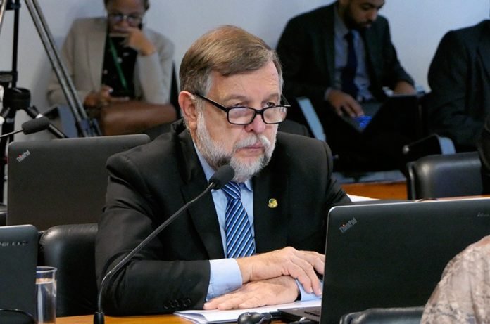 Descrição da imagem #PraCegoVer: O senador Flávio Arns durante sessão. Ele é um homem moreno, de pele clara. Tem os cabelos castanhos e barbas brancas. Flávio está usando terno preto, uma camisa azul claro e gravata azul com listras brancas. Ele está sentado em frente a um notebook e tem os braços cruzados sobre a mesa. Fim da descrição.