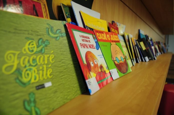 Descrição da imagem #PraCegoVer: Uma prateleira de madeira com vários livros infantis. Fim da descrição.