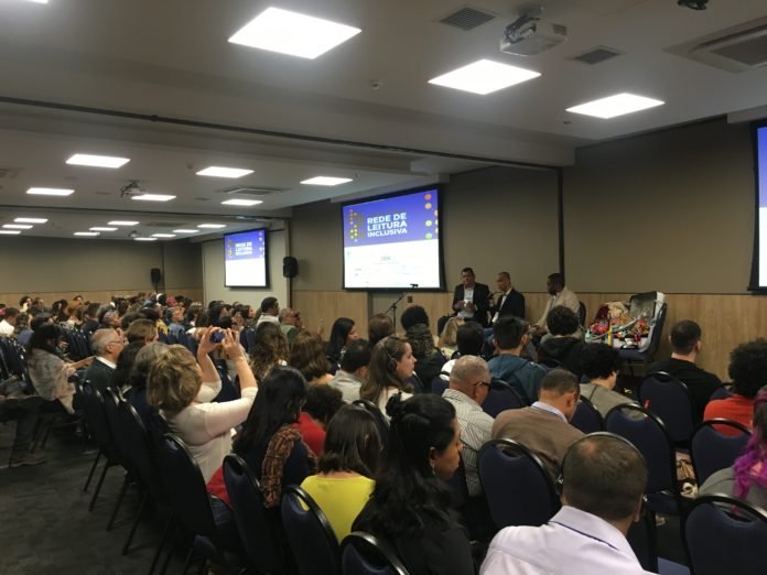 Descrição da imagem #PraCegoVer: Três homens estão sentados no palco do evento. Vemos, em primeiro plano, o público que acompanhou o bate-papo. Fim da descrição.