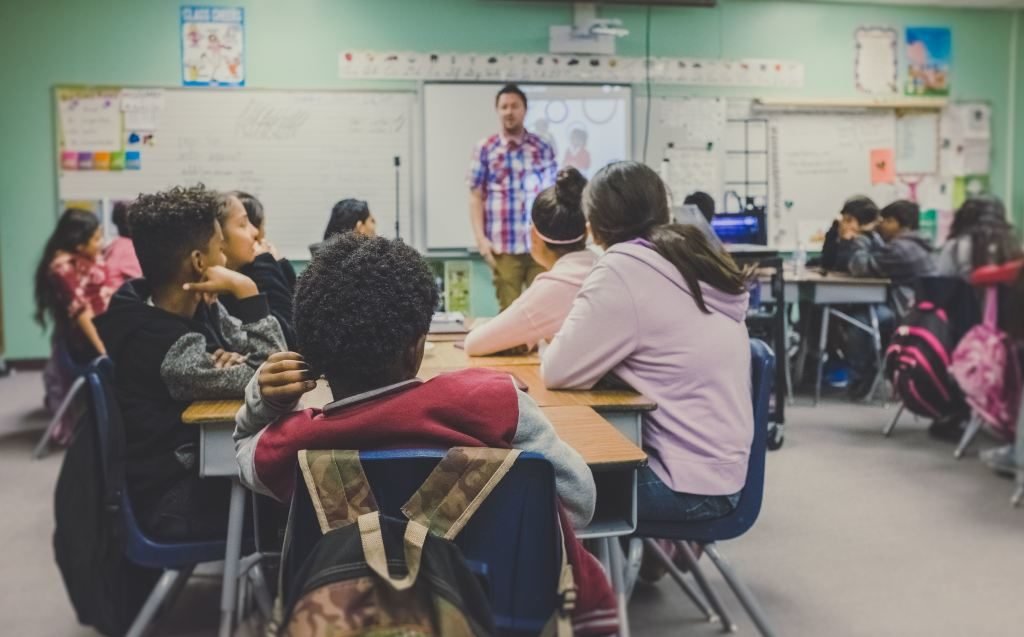 Descrição da imagem #PraCegoVer: Uma sala de aula com vários estudantes jovens que assistem a aula de um professor. Fim da descrição.