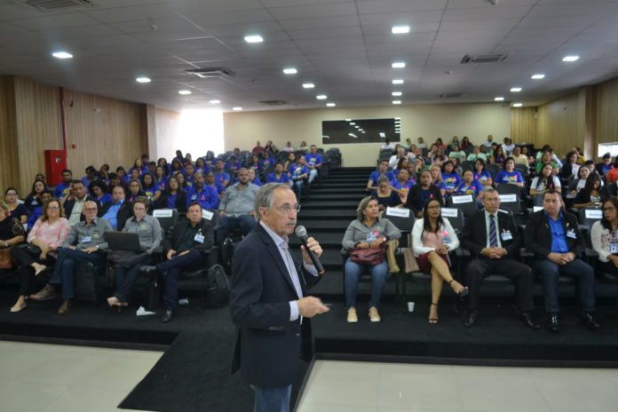 Descrição da imagem #PraCegoVer: Um senhor, de cabelos grisalhos, vestindo terno preto, está segurando um microfone. Ele está à frente de uma plateia cheia de pessoas. Fim da descrição.