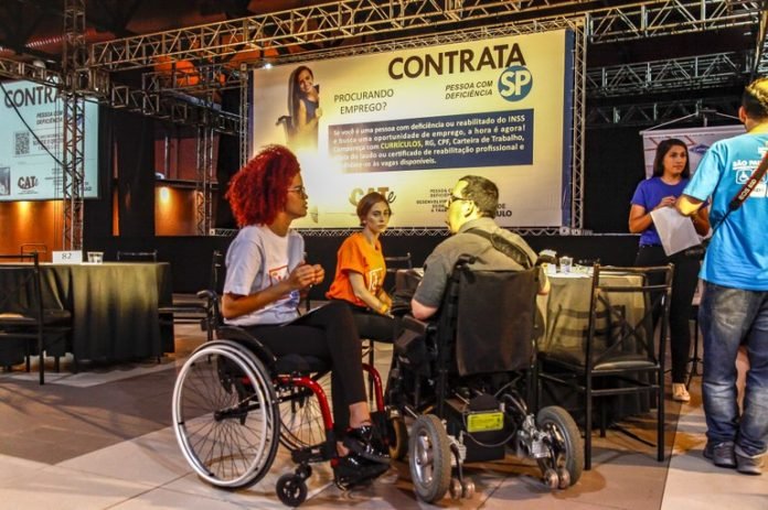 Descrição da imagem #PraCegoVer: Local onde foi realizado o Contrata SP. Em primeiro plano, estão: uma mulher e um homem, ambos cadeirantes, que estão conversando. Entre eles, mais ao fundo, está uma mulher. Fim da descrição.