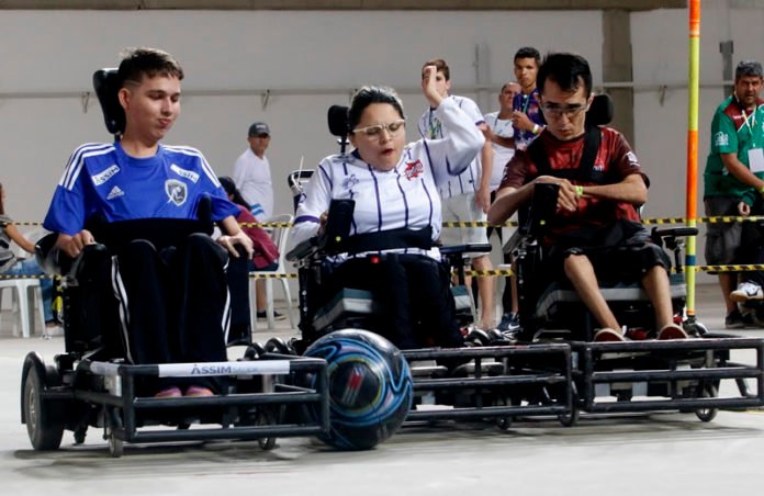 Descrição da imagem #PraCegoVer: Uma partida de Power Soccer. Na quadra vemos alguns atletas disputando a posse de bola. Fim da descrição.