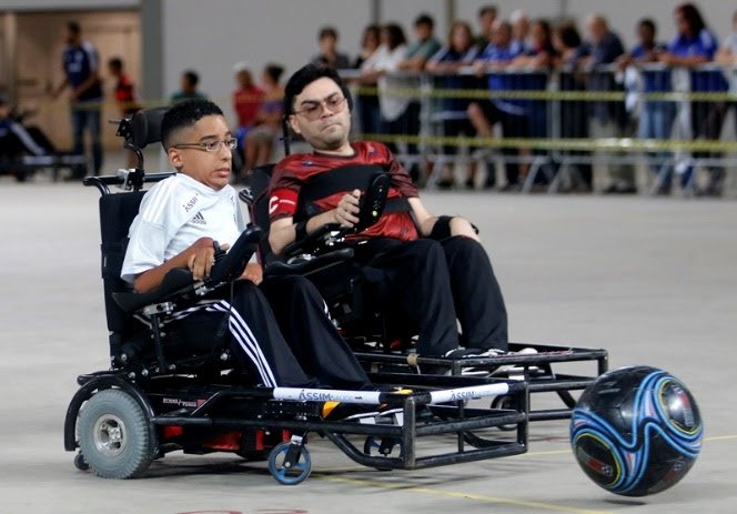 Descrição da imagem #PraCegoVer: Uma partida de Power Soccer. Na quadra vemos alguns atletas disputando a posse de bola. Fim da descrição.