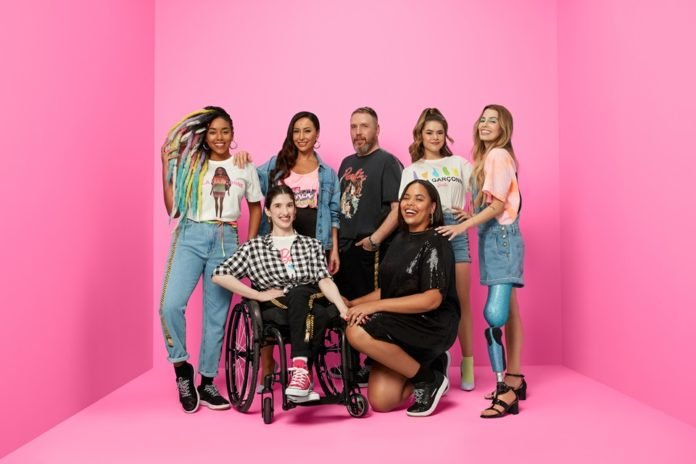 Descrição da imagem #PraCegoVer: Um grupo de mulheres, com e sem deficiência, estão ao lado do estilista Alexandre Herchcovitch. Entre elas está uma mulher cadeirante e uma mulher com uma prótese de perna azul. A imagem tem fundo rosa. Fim da descrição.