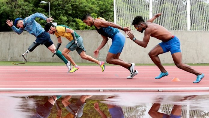 Descrição da imagem #PraCegoVer: Quatro paratletas estão na pista de atletismo do CT Paralímpico. Eles disputam uma prova de atletismo. Na parte inferior da imagem, uma poça d'água reflete a imagem dos atletas. Fim da descrição.