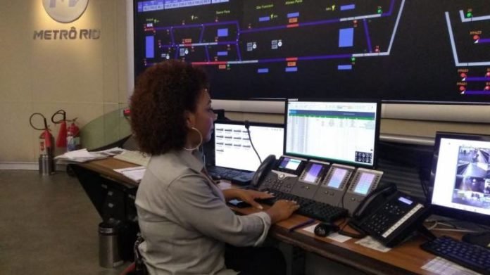 Descrição da imagem #PraCegoVer: A colaboradora Rosangela está na central de monitoramento do MetrôRio. Ela está sentada e, à sua frente, tem uma mesa com três monitores. Fim da descrição.