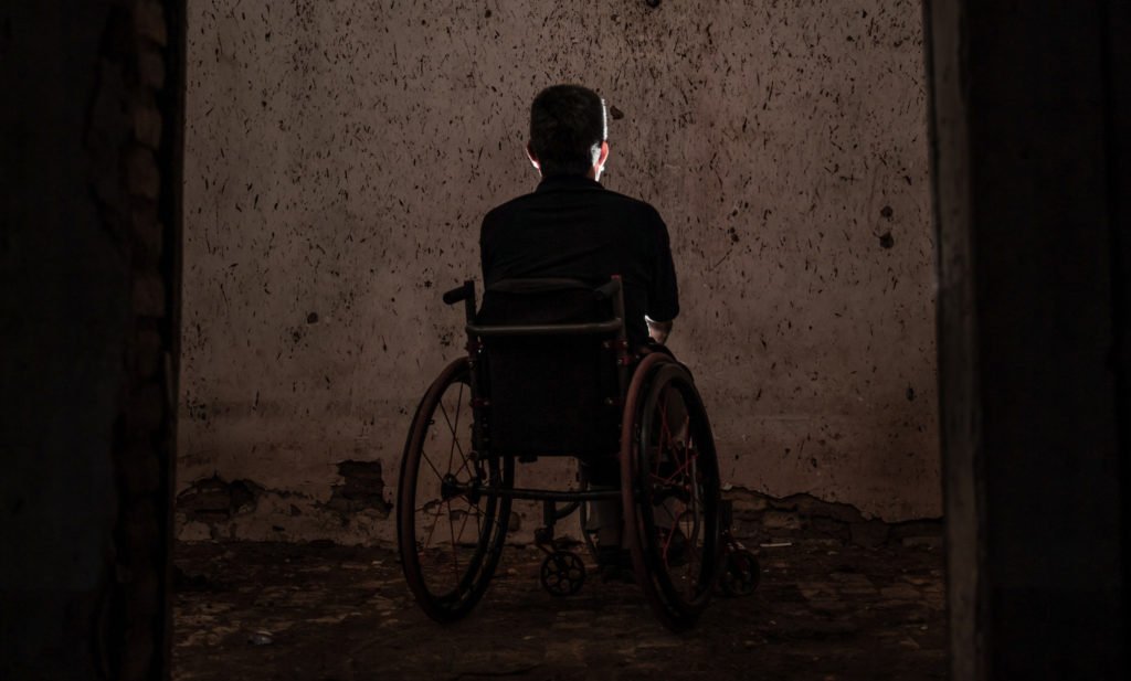 Descrição da imagem #PraCegoVer: Um homem cadeirante está sozinho, em um ambiente escuto. Fim da descrição