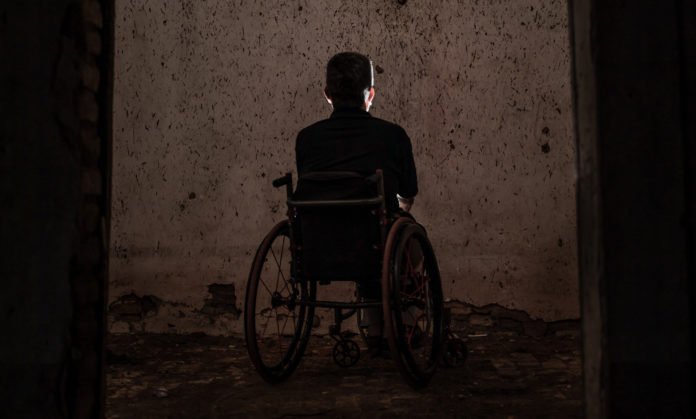 Descrição da imagem #PraCegoVer: Um homem cadeirante está sozinho, em um ambiente escuto. Fim da descrição