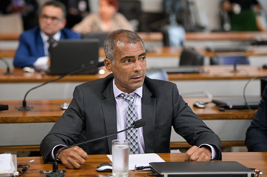 Descrição da imagem #PraCegoVer: O senador Romário está sentado em sua mesa na plenária do Congresso. Romário é um homem moreno, de cabelos grisalhos e ele está usando terno escuro, camisa branca e gravata quadriculada em preto e branco. Fim da descrição.