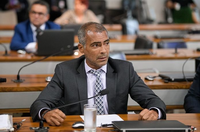 Descrição da imagem #PraCegoVer: O senador Romário está sentado em sua mesa na plenária do Congresso. Romário é um homem moreno, de cabelos grisalhos e ele está usando terno escuro, camisa branca e gravata quadriculada em preto e branco. Fim da descrição.