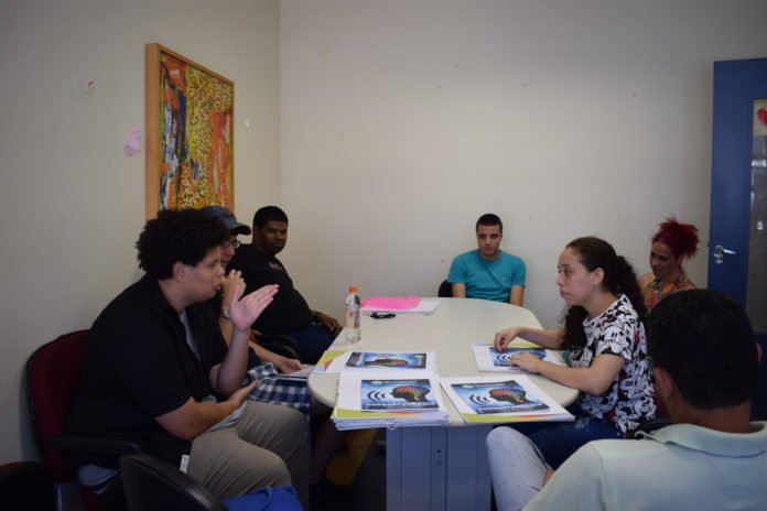 Descrição da imagem #PraCegoVer: Um grupo de jovens está sentado em volta de uma mesa. Eles discutem sobre o evento. Fim da descrição.