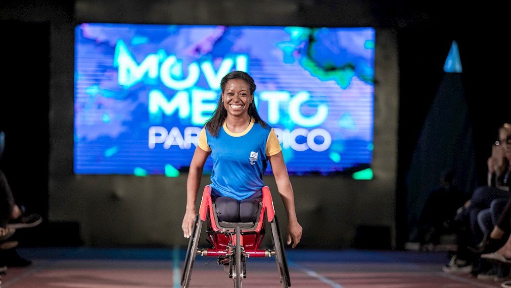 Descrição da imagem #PraCegoVer: A maratonista Vanessa Cristina. Ela está em sua cadeira de rodas. Vanessa é uma mulher negra, de cabelos pretos, compridos. Ela está usando uma camiseta azul com mangas amarelas. Vanessa sorri. Fim da descrição.