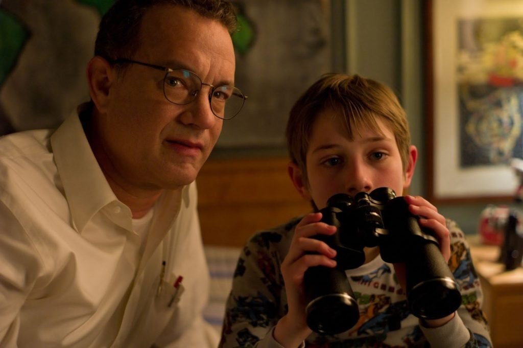 Descrição da imagem #pratodosverem: Cena do filme Tão forte, tão perto. Um menino e um homem estão lado a lado. O menino segura um binóculo. Fim da descrição.