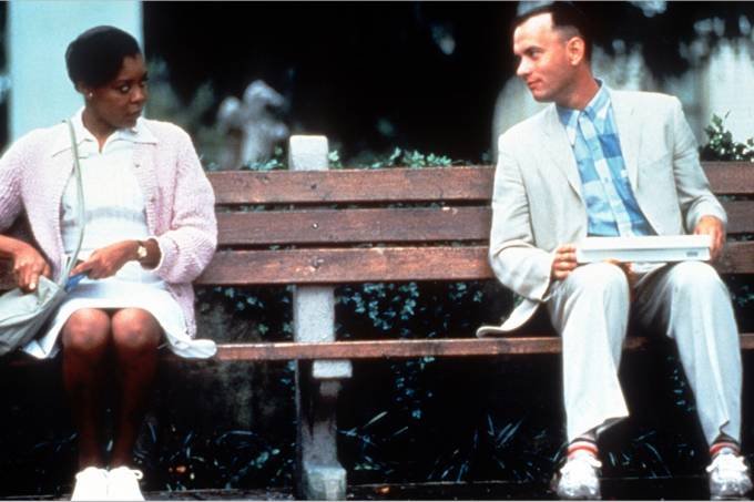 Descrição da imagem #pratodosverem: Cena do filme Forest Gump. Um homem e uma mulher estão sentados em um banco de praça. Fim da descrição.