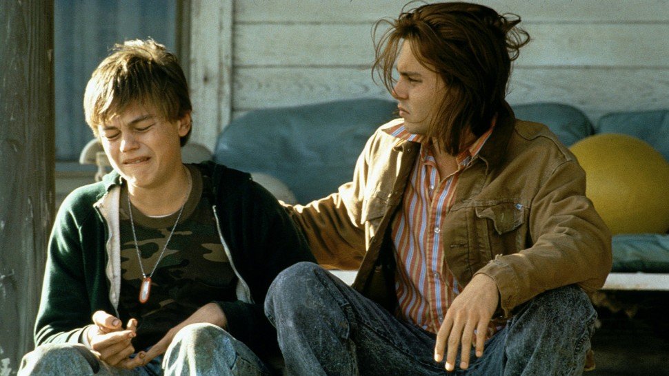 Descrição da imagem #pratodosverem: Cena do filme Gilbert Grape. Um menino e um rapaz estão sentados na porta de uma casa. O menino está chorando. Fim da descrição.