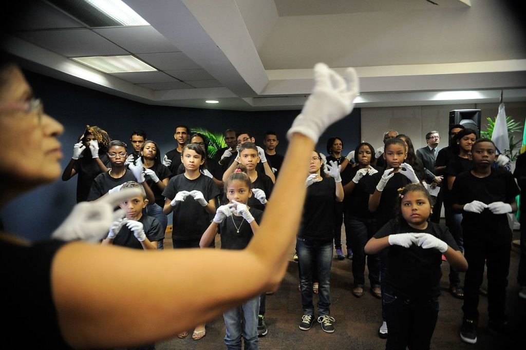 Descrição da imagem #PraCegoVer: Uma mulher coordena um coral em Libras. Fim da descrição.