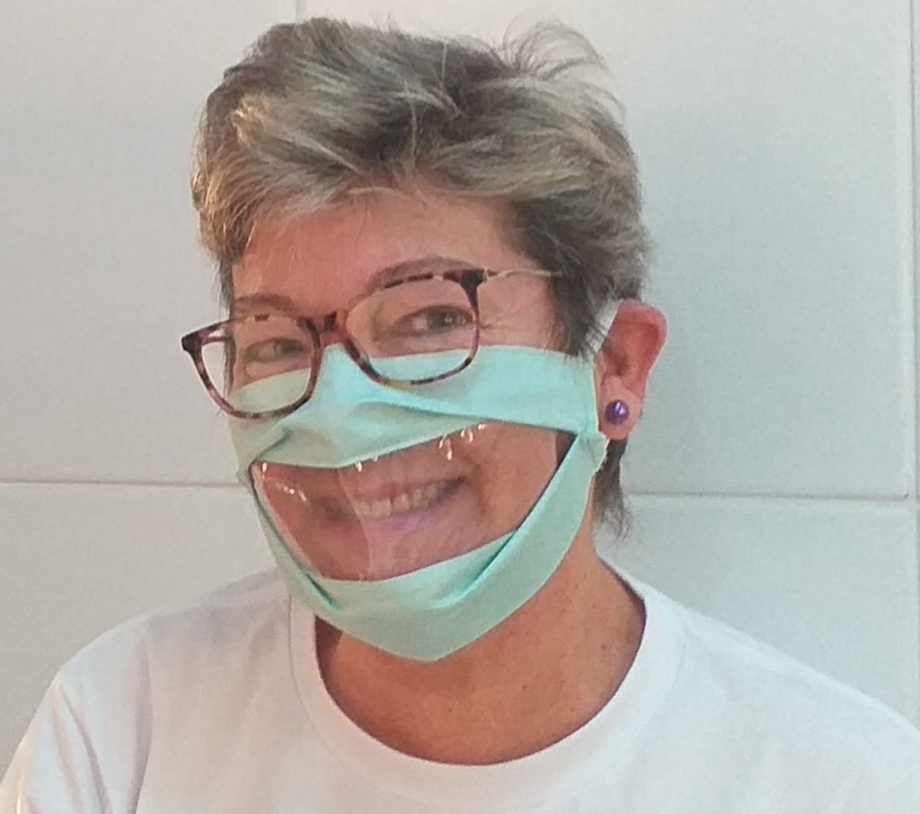Descrição da imagem #PraCegoVer: Uma mulher está usando a máscara adaptada, que tem uma abertura transparente na parte da boca. Fim da descrição.