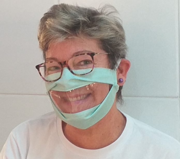 Descrição da imagem #pratodosverem: Uma mulher está usando a máscara adaptada, que tem uma abertura transparente na parte da boca. Fim da descrição.