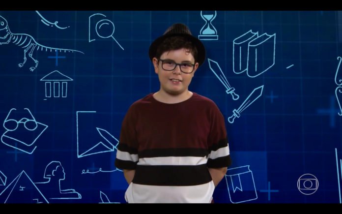 Descrição da imagem #pracegover: Foto do menino Pedro. Ele é moreno, tem pele clara e cabelos castanhos. Pedro usa uma camiseta bordô com listras brancas e pretas. Ele usa óculos e um chapeu preto. Ao fundo tem ilustrações de objetos relacionados à educação. Fim da descrição.