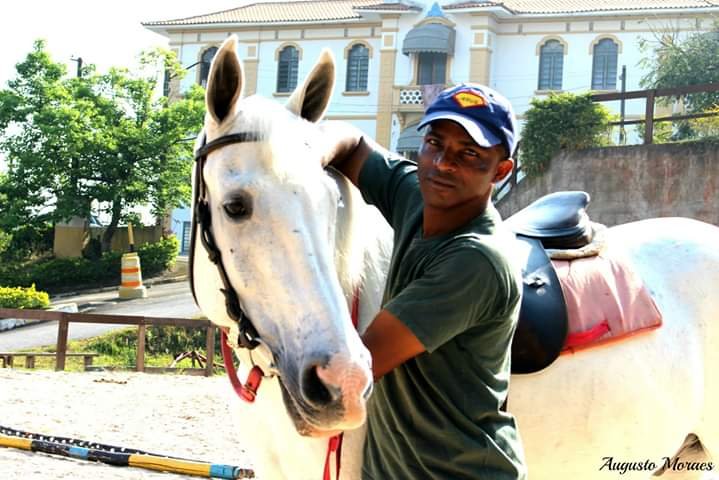 Descrição da imagem #pracegover: O auxiliar da equoterapia está abraçado a um cavalo branco. Fim da descrição.
