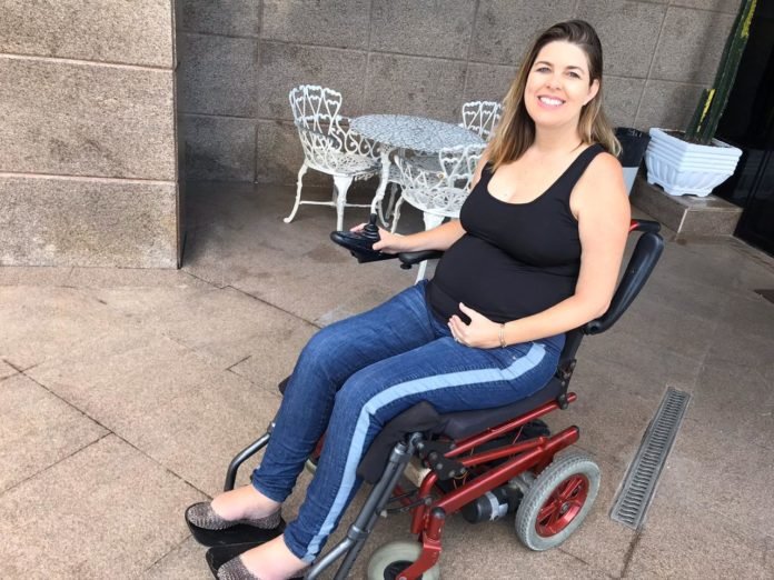 Descrição da imagem #pracegover: Ketly Vieira tem pele clara e cabelos lisos e loiros, um pouco abaixo dos ombros. Ela usa uma blusa preta e uma calça jeans. Ketly está em sua cadeira de rodas e sorri. Fim da descrição.