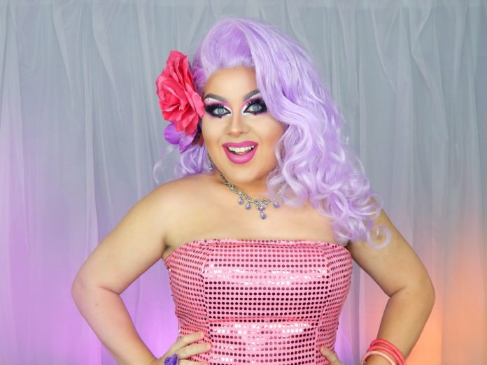 Descrição da imagem #pracegover: Foto da influenciadora digital Kitana Dreams. Ela é uma Drag Queen, branca, tem cabelos compridos lilás. Kitana está usando um tomara que caia pink de paetês e tem uma flor pink nos cabelos. Fim da descrição.