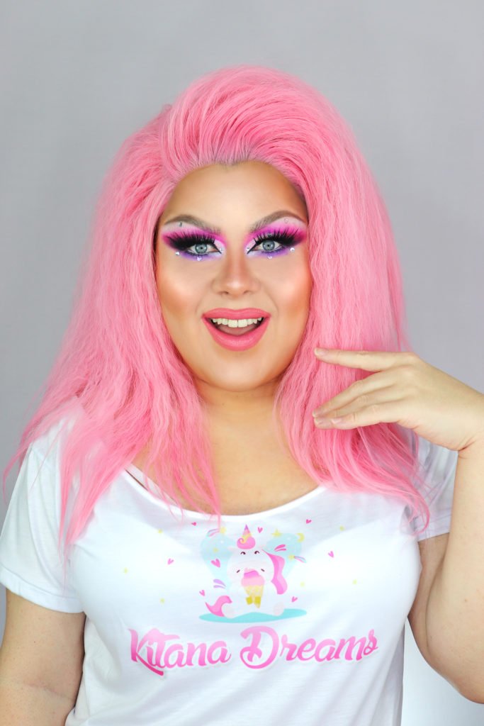 Descrição da imagem #pracegover: A influenciadora digital Kitana Dreams. Ela é uma Drag Queen, branca em que está escrito: Kitana Dreams. Ela tem cabelos compridos cor de rosa. Kitana está usando uma blusinha branca. Fim da descrição.